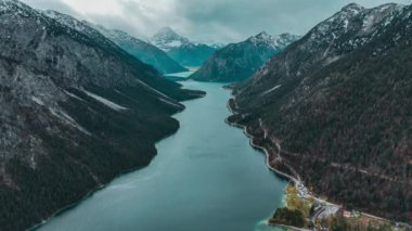 Avusturya 'nın Tyrolean Alpleri' ndeki kar örtülü dağların arasında sonbaharın sonlarında bulutlu havada uçan drone gölü görülüyor. Yüksek kalite 4k görüntü