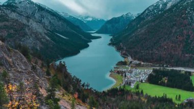 Avusturya 'nın Tyrolean Alpleri' ndeki kar örtülü dağların arasında sonbaharın sonlarında bulutlu havada uçan drone gölü görülüyor. Yüksek kalite 4k görüntü