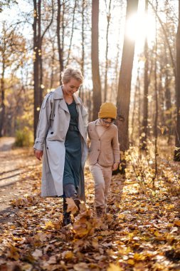 Happy mom and child son in warm clothes walking in autumn park in nature in fall outdoor. attractive short-haired lady enjoy spending time with son. holidays, weekends, childhood concept