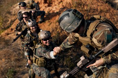 command rangers soldiers during the military operation. soldiers climbing on mountain, one of them giving hand and helping to climb. Help, support, assistance in a dangerous situation
