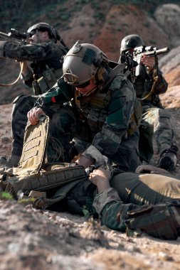 military man use military first aid kit for saving life of injured comrade on battlefield, sick man is lying on ground. brave and friendly guy in military clothes help friend, risky situations