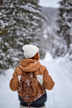 Rear view On Good-looking Lady In Warm Outfit Walking In Winter Forest Alone, Enjoying The view. Beautiful Caucasian Lady With Backpack Stand Taking A Break During Walk, Hike. Recreation Concept