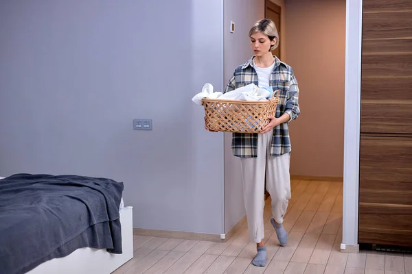 stock image Woman in casual domestic outfit doing the daily chores laundry, alone at home indoors. beautiful young Female housewife folded clothes in laundry basket. Laundry, House work, Chores concept.