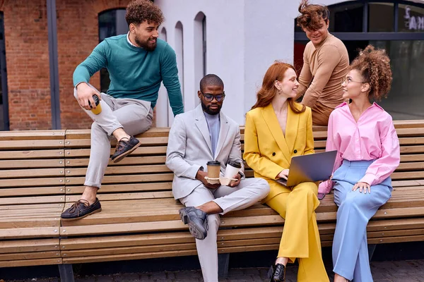 Group portrait of interracial diverse young multiethnic businesspeople posing together sitting in bench, happy motivated multiracial employees show unity and success, teamwork, cooperation concept