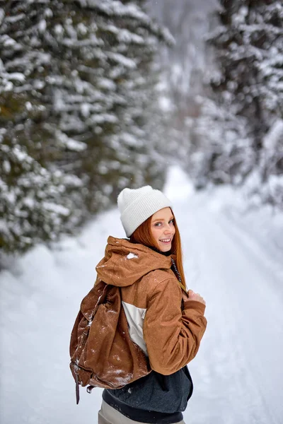 Good-looking Red-haired Woman In Stylish Warm Coat With Backpack Walking In Wonderful Winter Forest Alone, Outdoors. Healthy Lifestyle, Recreation, Travel, Hiking, Happiness, Adventure Concept