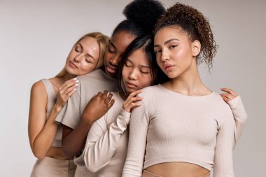 Sleepy diverse female models are posing in beauty shooting, leaned on each other. Calm and pacified women in casual outfit. Black american, asian, caucasian european appearance, natural beauty