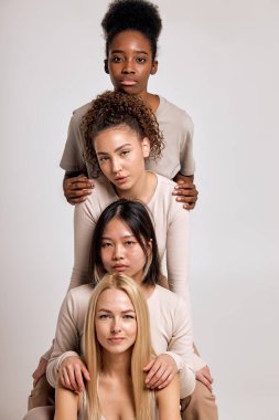 four women with different hair and skin color posing in studio, confident in themselves, dressed casually, friendly and nice. black american, asian and european models indoors, portrait. in a row