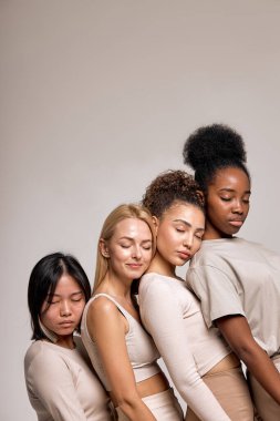 Sleepy and calm diverse women models leaned on each other posing, with eyes closed, isolated on beige studio background, portrait copy space. natural beauty, calmness, confidence concept