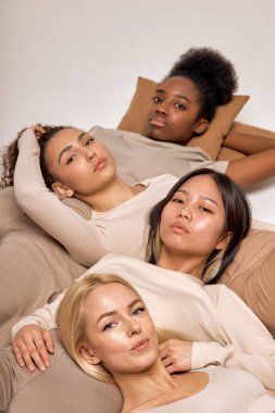 models being very close one to each other, lying on floor, expressing friendship and tolerance. attractive beautiful women in casual outfit looking relaxed. indoor shot, top view. focus on blonde