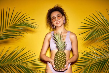 portrait of funny funky fancy style stylish lady holding pineapple in hand isolated on vivid yellow studio background. attractive caucasian lady in fashionable sunglasses, relax enjoy summer