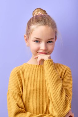 Hmm. Let me think. Studio shot of pretty blonde girl with hair knot and looking ar camera with thoughtful and sly expression, planning and thinking something. isolated on purple
