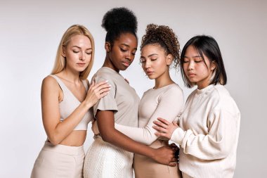 group of beautiful multiracial young women with different ethnicity and skin posing together. Pacified black american asian and caucasian ladies leaned on each other, calm. Isolated on white