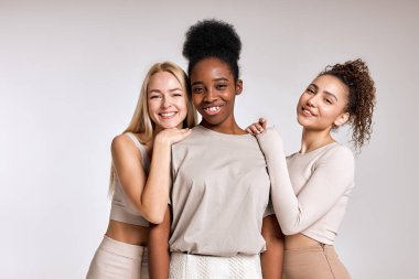 three diverse beautiful models are posing on white background. Close-up portrait of young women in casual outfit posing at camera together, looking happy, cheerful. copy space. black, caucasian