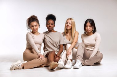 Portrait of diverse group of women sitting on floor, young females in basic clothing look at camera, having rest, friendly women have different race and skin, hair colour. natural beauty concept