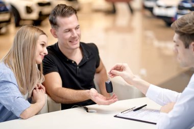 cropped Manager giving keys by new car to caucasian couple buyers, purchasing automobile together, male becoming owner of first car shared property with wife. Ownership, sales concept