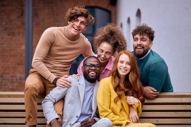Business people in formal suit having fun together spending time in street of city, looking excited, happy men and women of diverse interracial ethnicities sit on bench enjoying leisure. portrait