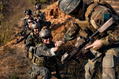 brave command rangers soldiers during the military operation. soldiers climbing on mountain, one of them giving hand and helping to climb. Help, support, assistance in a dangerous situation