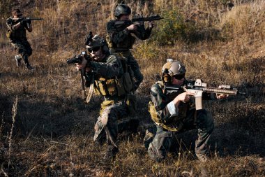 Group of army soldiers outdoors, marines group in action, shooting with assault rifle and machine gun, attacking enemy. Young caucasian men in military uniform concentrated on fight