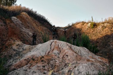 Squad of Fully Equipped Soldiers in Camouflage on Reconnaissance Military Mission, Wearing Military Clothes Equipment. Brave And Strong Guys With Rifles Guns On Hot Spot During Operation