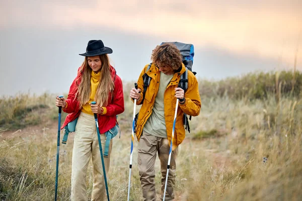 couple with bag pack on back holding trekking pole during hiking jurney, active athletic man and woman in colorful sportive outfit, vacation in nature outdoors. travel, sport, adventure concept