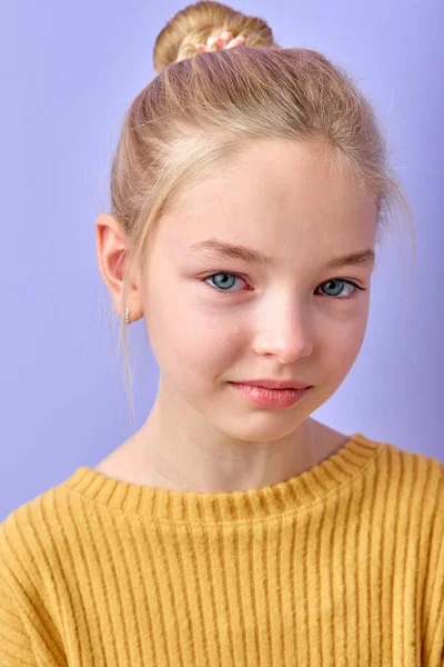 Portrait of beautiful young blonde woman crying with tears smiling on camera in studio on purple background. Charming cute child in yellow shirt is stressed, sad and offended