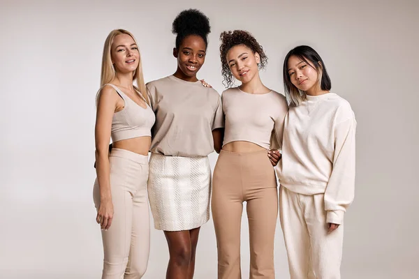 Natural beauty, diversity concept.Four multiethnic young women, Caucasian, Black and Asian, with diffrent types of skin, posing together against studio background and looking at camera