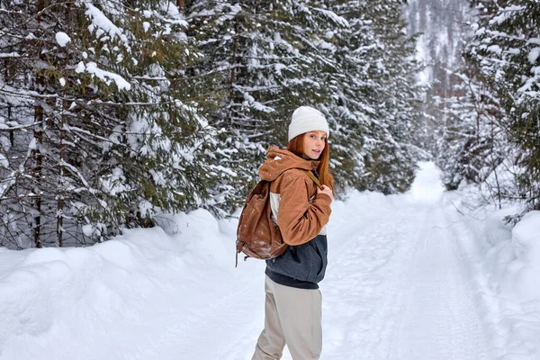Attractive Red-haired Woman In Stylish Warm Coat With Backpack Walking In Wonderful Winter Forest Alone, Outdoors. Healthy Lifestyle, Recreation, Travel, Hiking, Happiness, Adventure Concept