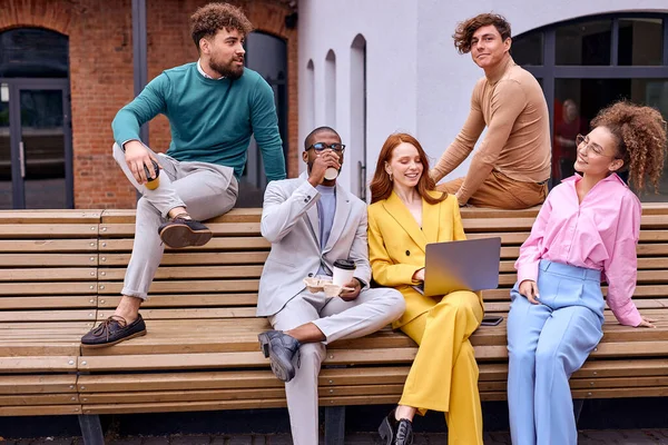 Group portrait of smiling diverse young multiethnic businesspeople posing together sitting in bench, happy motivated multiracial employees show unity and success, teamwork, cooperation concept