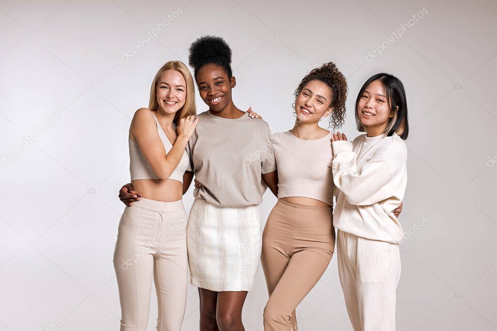 Natural beauty, diversity concept.Four multiethnic young women, Caucasian, Black and Asian, with diffrent types of skin, posing together against studio background and looking at camera