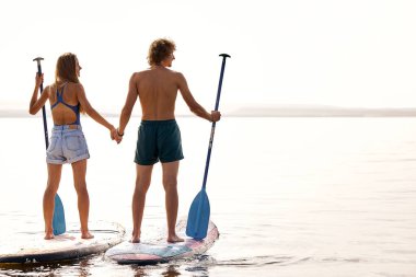 rear view on couple man and woman standing on surfboard taking break, having rest, young caucasian man and woman enjoy free time together, spend weekends on lake or river. sport, people lifestyle