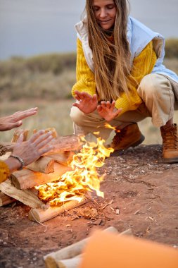 warming hands above the bonfire. evening time, rest. Selective focus. cropped people sit next to fire enjoying camping, trekking. holidays in nature