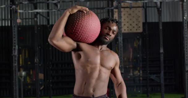 カメラを見て肩にフィットボールを持っているドレッドを持つ深刻な筋肉の無気力な男 スローモーションライフスタイルホビーボディケアウェルネス強度トレーニング — ストック動画