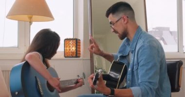 Yetenekli erkek öğretmen gitar çalmayı öğretiyor, iki parmağını gösteriyor, sohbet ediyor, yavaş çekimde sohbet ediyor. kendi şarkılarını öğrenmek eğitim mücadelesi