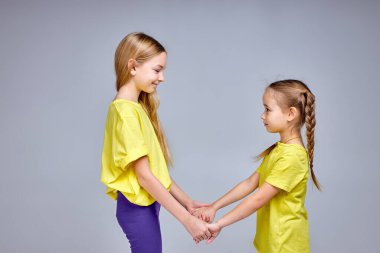 Ablası ufaklığı eğlendiriyor. Gülümseyen iki harika çocuk stüdyoda eğleniyor. Çember yapmak, el ele tutuşmak, şarkı söylemek, dans etmek, soyutlanmış beyaz arka plan