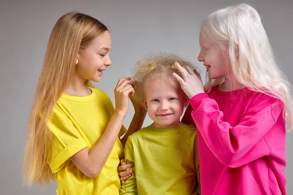 two girls touching their friends fluffy, wavy, curly hair, sisters doing hair to their little sister isolated white background, hairstyle fashion