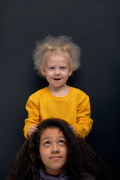 funny little girl with fair fluffy hair doing her sister hair, blonde kid touching her friend hair, head, creation of fashion stylish hairstyle free time, hobby, fun