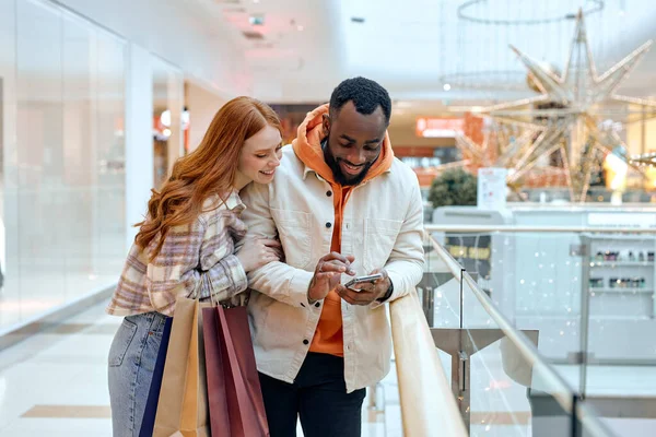 使用手机的年轻人手持彩色购物袋站在商场里快乐的顾客使用应用程序购买衣服在线智能手机 电子商务短视主义 免费业余时间 — 图库照片