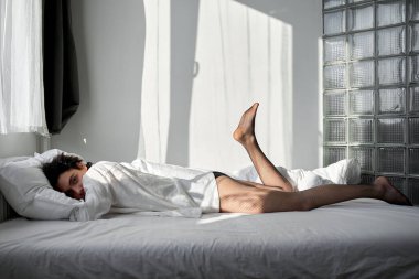 İpek beyaz yatakta yatan seksi adam. Tam boy yan görüş. Erkek kameraya bakar. Boş zaman, boş zaman, yaşam tarzı