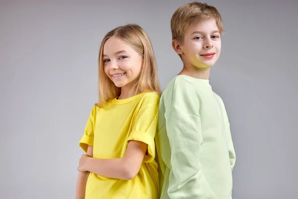 two adorable kids, sister and brother standing back to back looking at camera, isolated white background. childhood, relatives