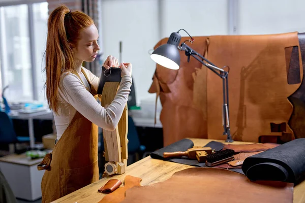 professional female artisan working on Leather Stitching Clam side view shot.handmade technique, active ginger beautiful girl creating her own wallet