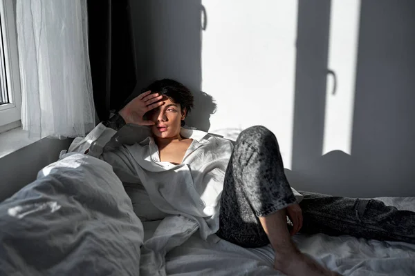 悲しい眠いブルネットの若いハンサムな男がベッドの上に横たわっている 偏頭痛 朝のオーバーハング 不幸な不健康な男 — ストック写真