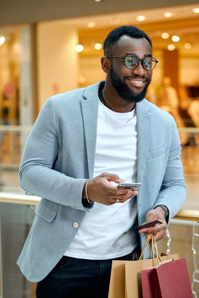 Stock image Happy smiling handsome young bearded man holding smartphone, card and colorful shopping bags.happiness, man buying goods online, close up side view photo.shopping addiction.