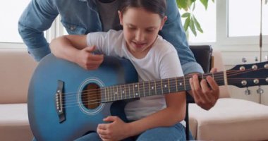 Evde yeni başlayanlar için gitar dersi alan sevimli bir çocuk. Adam kızın arkasında duruyor ve akor çalmak, davul çalmak, yavaş çekim gibi temel şeyleri öğretiyor.