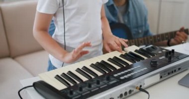 Küçük yetenekli kız synthesizer çalmayı öğreniyor, arka planda gitar çalan sakallı yakışıklı adam, müzikal ikili prova, stüdyoda, evde, yavaş çekimde, yakın çekimde şarkı söyleme pratiği