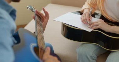 Öğretmen, öğretmen, öğrenci egzersiz kitabı yazarken gitar çalan öğretmen, kırpılmış videoyu kapat. Yavaş çekim, kadın gitarist kalemle not alıyor. Müzik bestecileri metni düşünüyor.