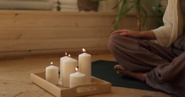 Kadın mumları üflüyor, yoga yapıyor lotus pozisyonunda oturuyor mumların yanında meditasyon yapıyor tütsü yakıyor, kadın meditasyon yapıyor zemin zumunda oturuyor, dindarlık ruhsallığı yavaş çekimde kesiliyor.