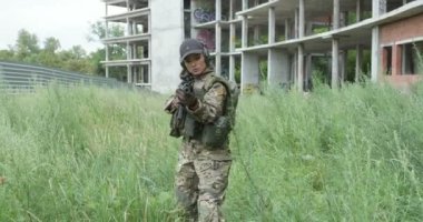 Kamuflajlı kadın kendine güvenen asker uzun otların arasında yürüyor ve tüfekleri doğrultuyor, arkadaşlarıyla oyun oynuyor, rakip arıyor, eğlendiriyor, yavaş çekim yapıyor.