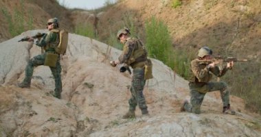 Kamuflajlı, el bombası atan bir grup erkek asker, tehlike altındaki askeri görev sırasında tepedeki düşman karakoluna sis bombası atarak saldırıyor.