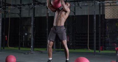 Sporcu, kaslı, siyah sakallı bir adam spor salonunda ilaç topuyla çalışıyor. Güçlü bir adam spor hedeflerine yavaş çekim motivasyon yarışmasına katılıyor.