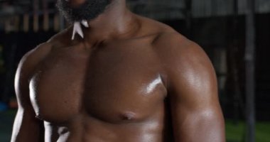 Güçlü, atletik, Afro-Afrikalı, boncuklu, terli, göğüs kaslı, ağır çekimde kaslı gülümseyen bir adamın yakın çekimi.